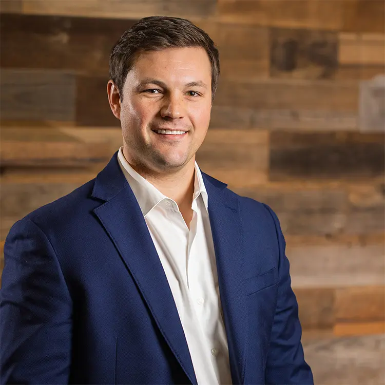 Colby Photo A man in a suit standing next to a wooden wall.